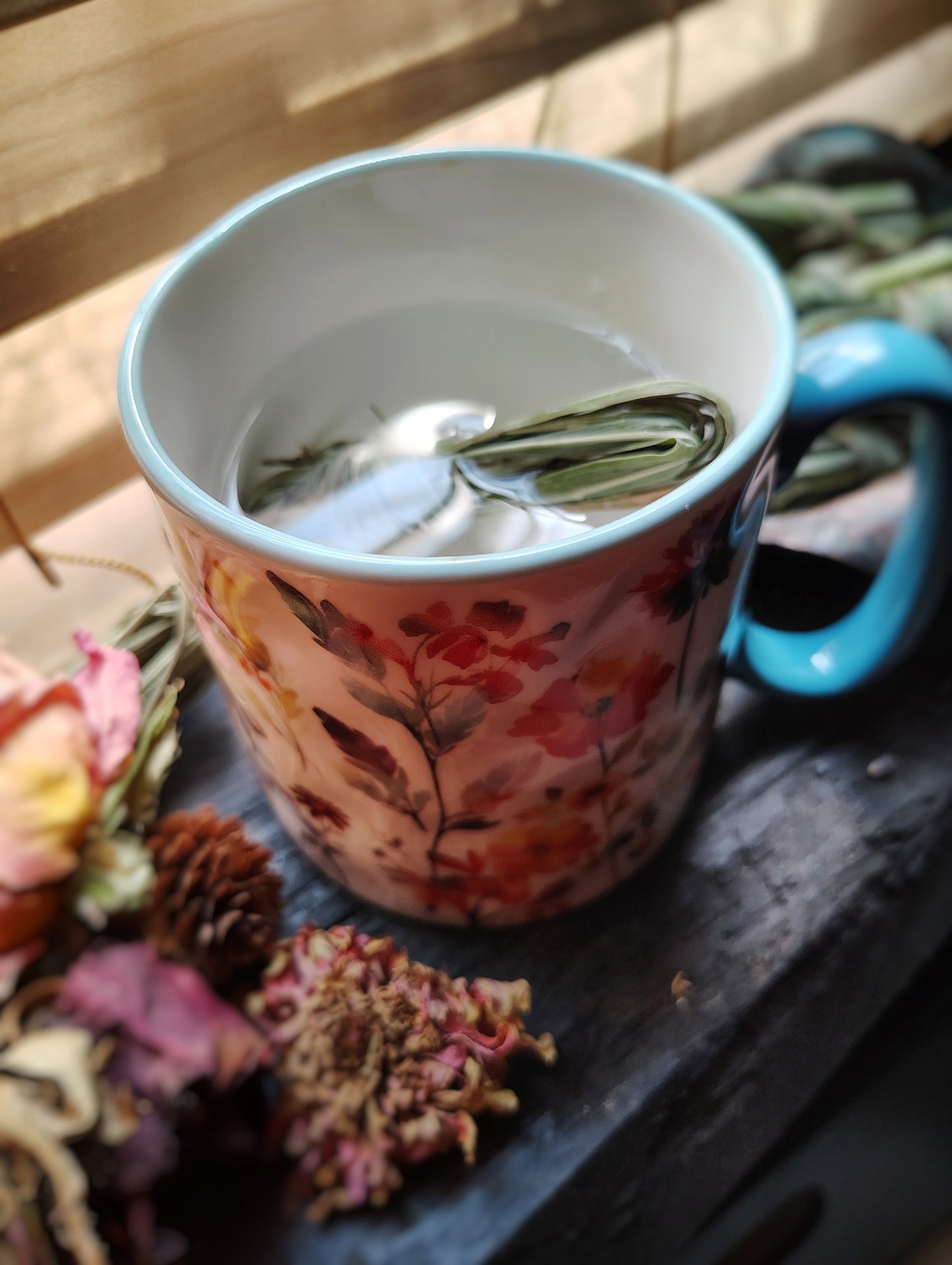 Tea cup with floral design containing a lemongrass bundle on a wooden surface.