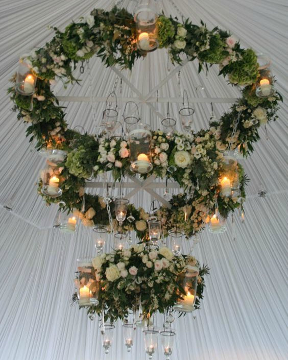 Decorative chandelier with smilax greenery, floral arrangements, and candles on a white ceiling.