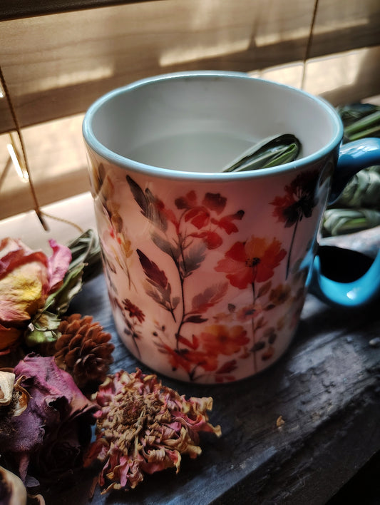 Decorative mug with floral design on a wooden surface with dried flowers.